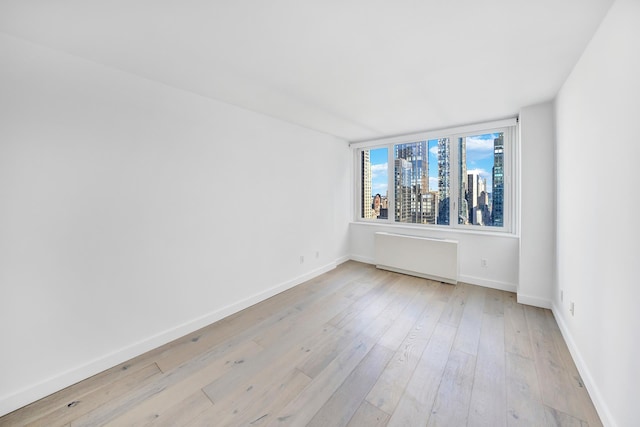 unfurnished room featuring baseboards, a city view, radiator heating unit, and light wood-style floors