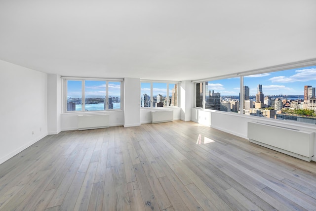 unfurnished living room with a city view, hardwood / wood-style floors, baseboards, and radiator heating unit