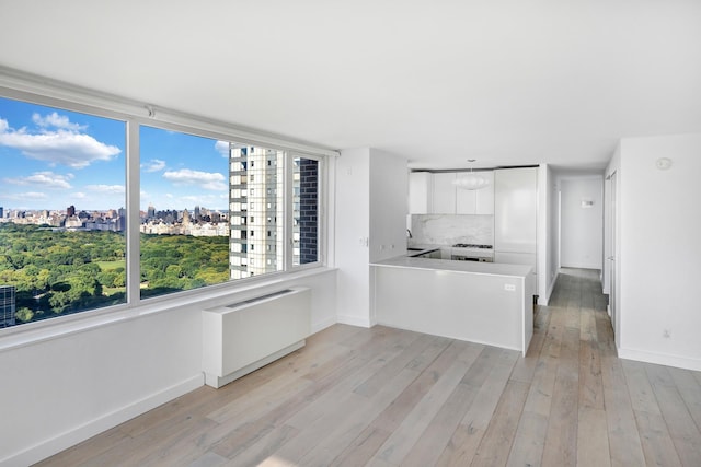 kitchen featuring a view of city, light wood finished floors, backsplash, radiator heating unit, and white cabinets