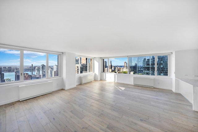 unfurnished living room featuring radiator heating unit, a view of city, light wood finished floors, and baseboards