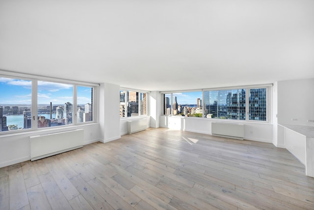 interior space featuring light wood-type flooring, baseboards, a city view, and radiator heating unit