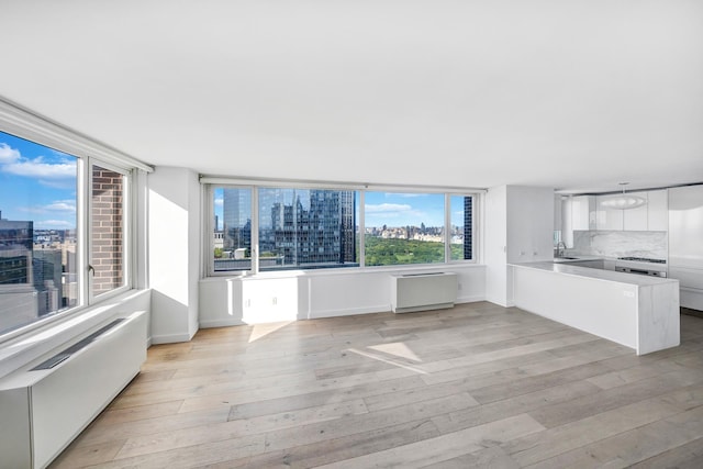 unfurnished living room featuring a sink, light wood finished floors, baseboards, and a city view