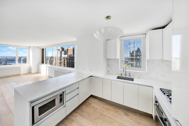 kitchen featuring stainless steel appliances, white cabinets, a sink, light wood-type flooring, and a peninsula