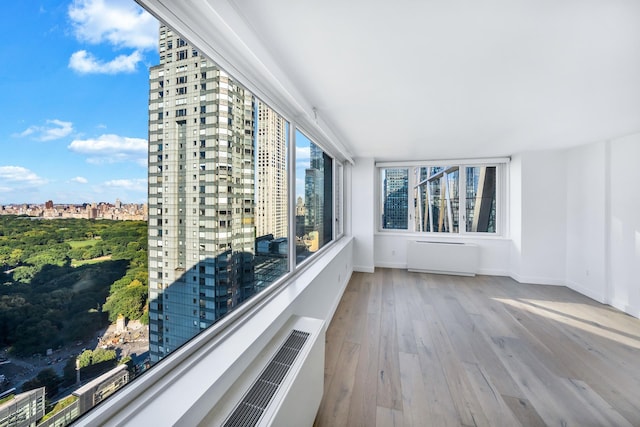 unfurnished sunroom featuring a city view, plenty of natural light, and radiator heating unit