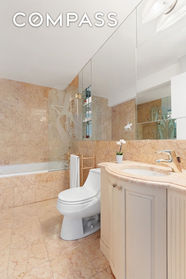 bathroom featuring tiled shower / bath, toilet, marble finish floor, tile walls, and vanity