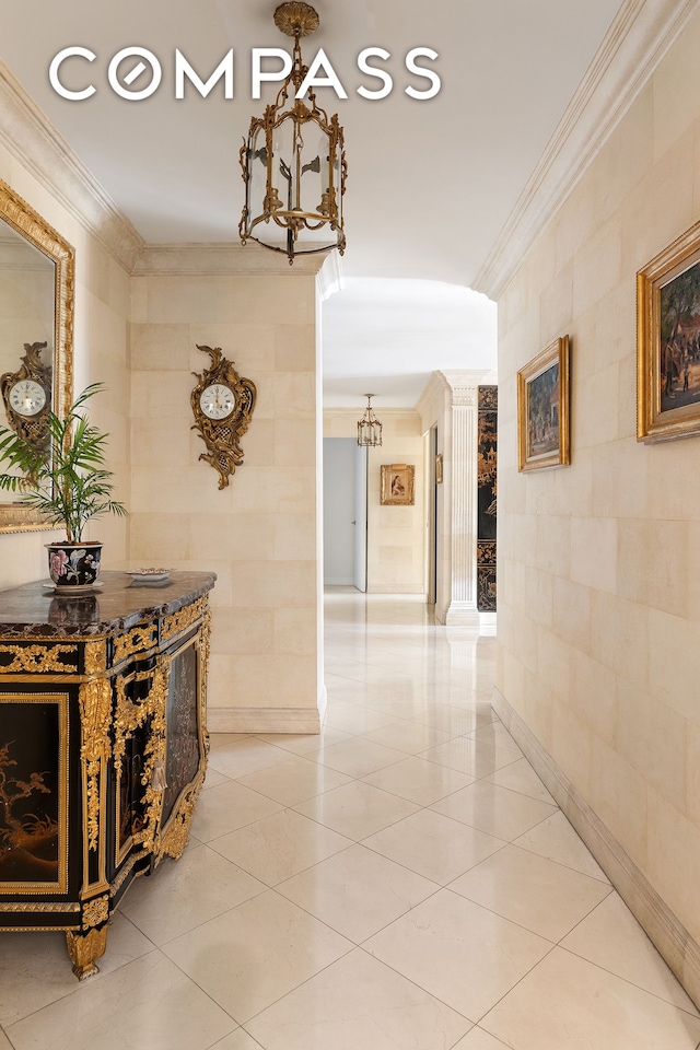 hallway featuring light tile patterned floors, ornate columns, an inviting chandelier, ornamental molding, and tile walls