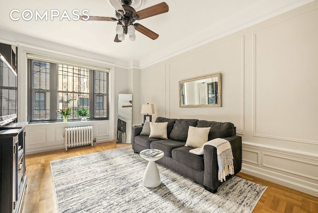 living room with crown molding, ceiling fan, radiator heating unit, a fireplace, and light parquet flooring