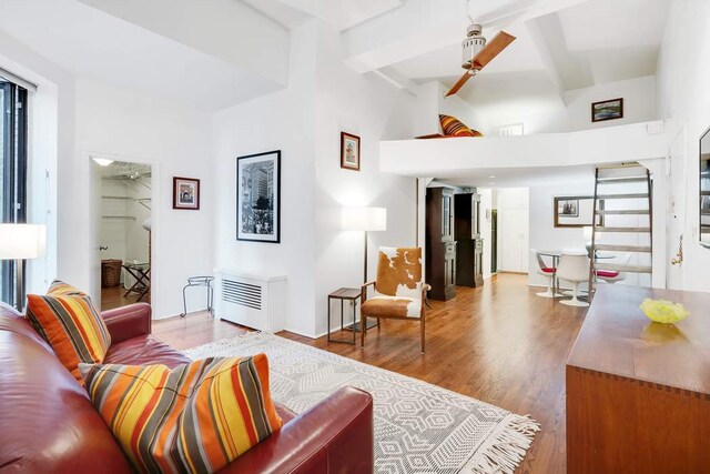 living room featuring beamed ceiling, ceiling fan, wood-type flooring, and radiator