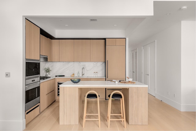 kitchen featuring a breakfast bar area, stainless steel appliances, light countertops, backsplash, and light brown cabinetry