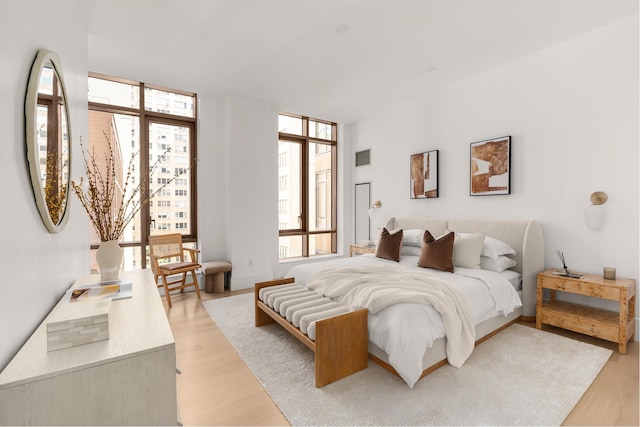 bedroom with floor to ceiling windows, light wood-style flooring, and multiple windows