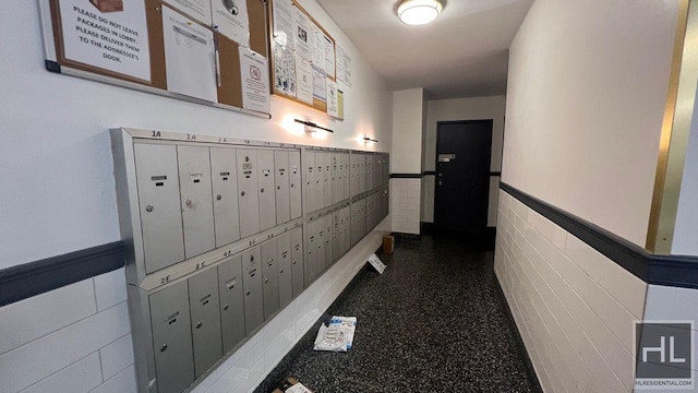 hallway with wainscoting, mail area, and tile walls