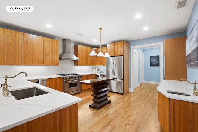 kitchen featuring wall chimney range hood, light stone counters, stainless steel appliances, and a sink