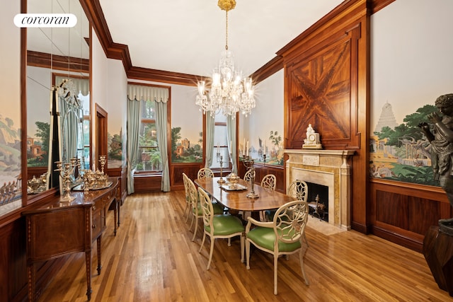 dining room with wainscoting, light wood-style flooring, a premium fireplace, ornamental molding, and a chandelier