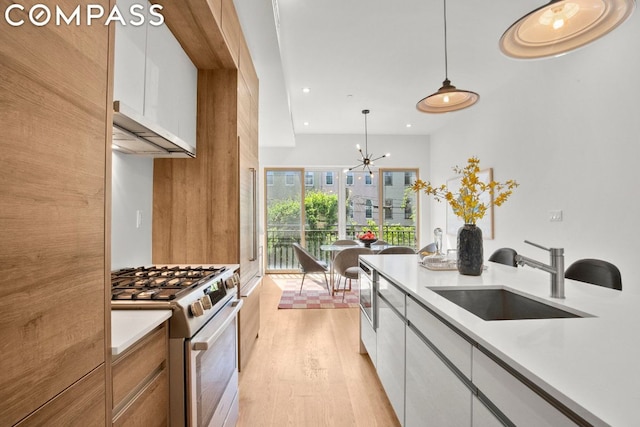 kitchen with pendant lighting, sink, stainless steel gas stove, white cabinetry, and a chandelier