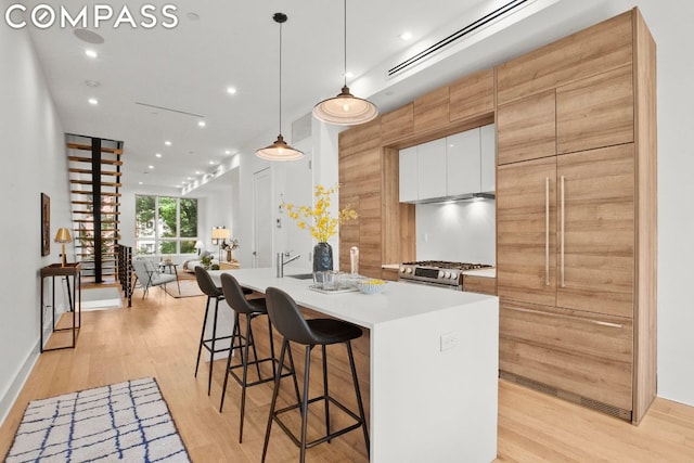 kitchen with stainless steel range with gas cooktop, white cabinets, pendant lighting, light hardwood / wood-style flooring, and sink