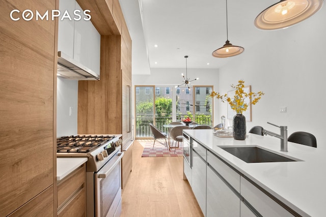 kitchen featuring decorative light fixtures, stainless steel gas range, light countertops, light wood-type flooring, and a sink