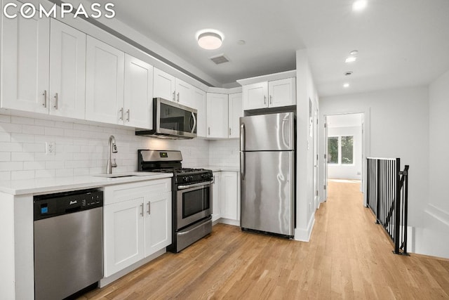 kitchen featuring appliances with stainless steel finishes, sink, white cabinets, decorative backsplash, and light hardwood / wood-style floors