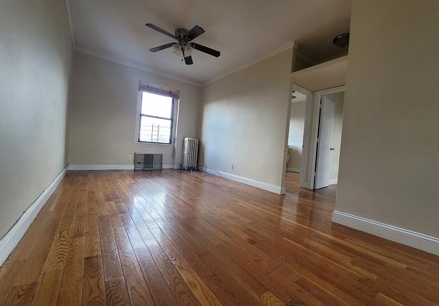 empty room with radiator, baseboards, hardwood / wood-style floors, ornamental molding, and a ceiling fan