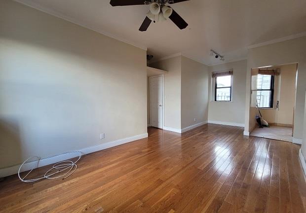 spare room featuring baseboards, wood-type flooring, ornamental molding, and a ceiling fan