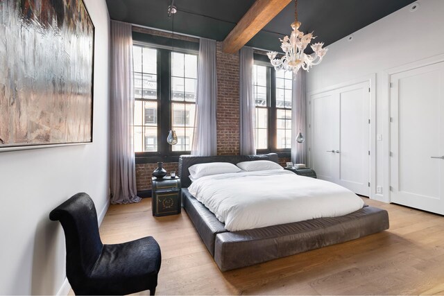 bedroom with a chandelier, beamed ceiling, light wood-style flooring, and brick wall