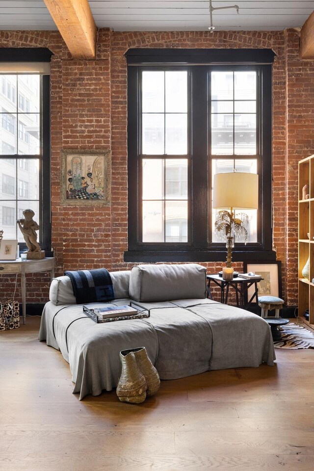 bedroom featuring beamed ceiling, brick wall, and wood finished floors