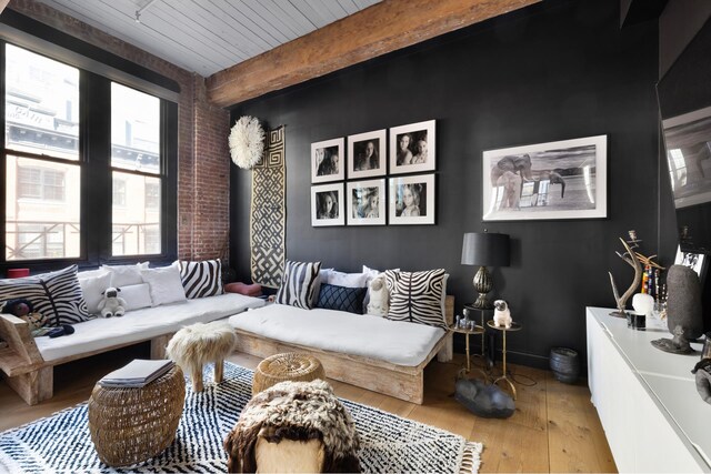 interior space featuring hardwood / wood-style flooring, brick wall, baseboards, and beam ceiling