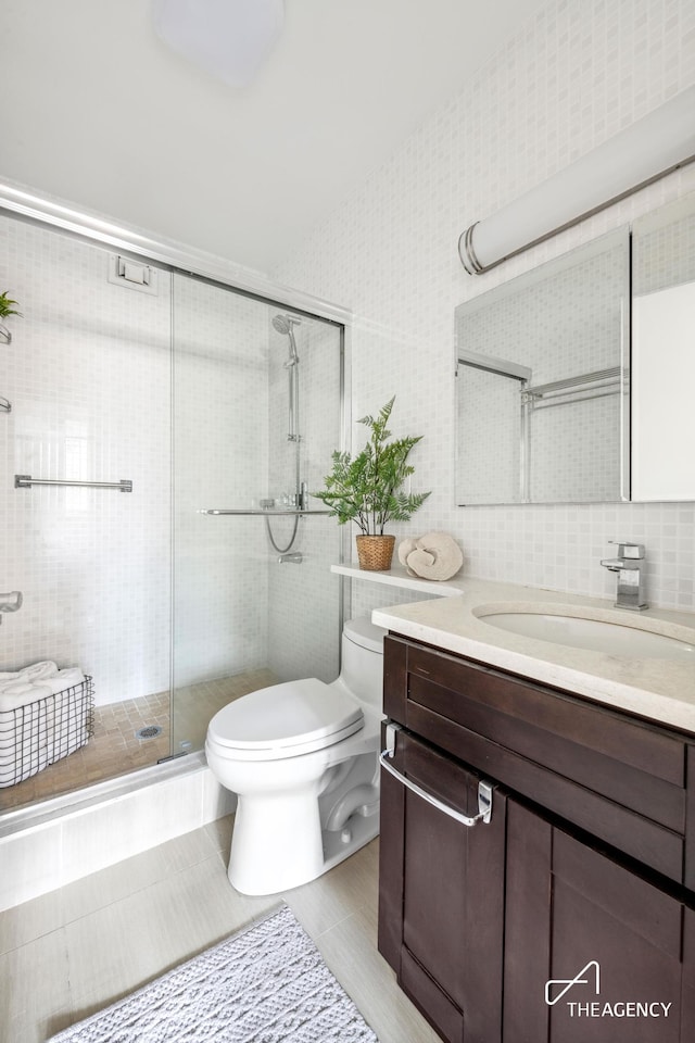 full bath with a stall shower, toilet, tile patterned floors, vanity, and tile walls