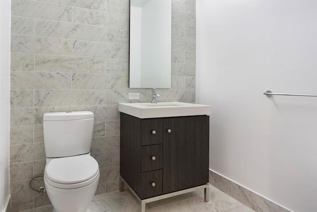 bathroom featuring toilet, marble finish floor, tile walls, and vanity