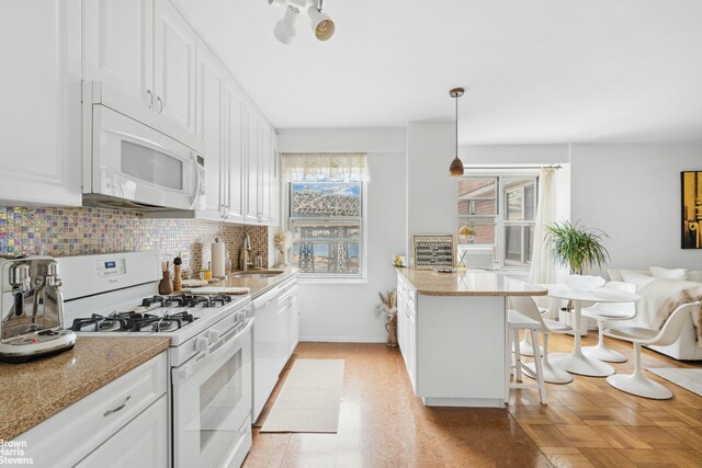 kitchen with hanging light fixtures, white appliances, a kitchen breakfast bar, and white cabinets