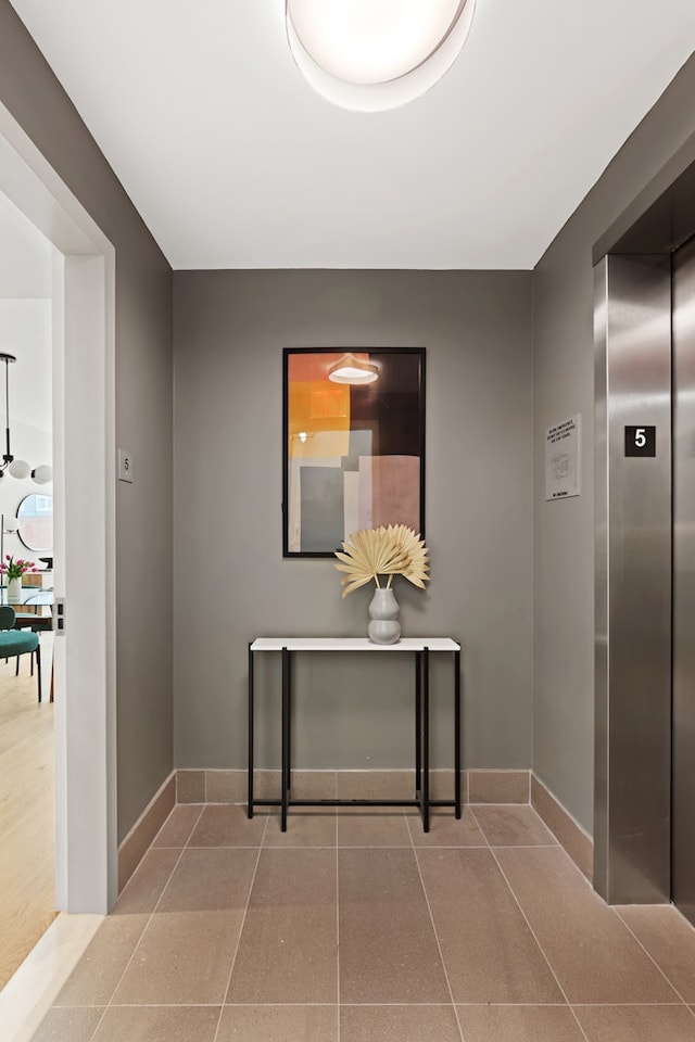 corridor featuring baseboards, elevator, and tile patterned flooring