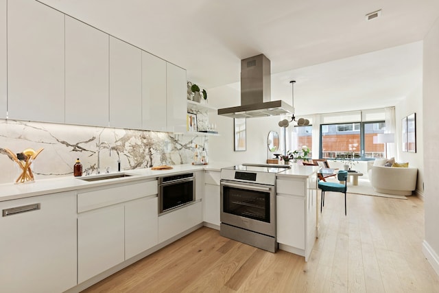 kitchen featuring stainless steel appliances, light wood-style flooring, a sink, a peninsula, and exhaust hood