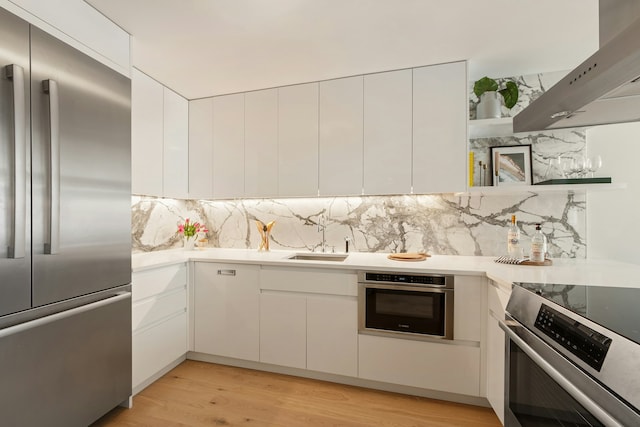 kitchen with stainless steel appliances, exhaust hood, a sink, white cabinetry, and light countertops