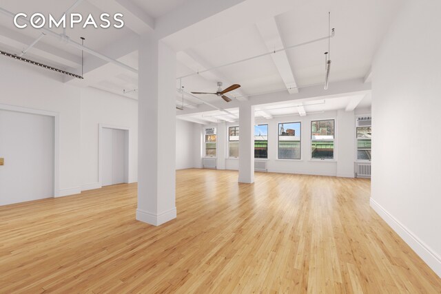 unfurnished living room featuring radiator, baseboards, beamed ceiling, light wood-style floors, and a ceiling fan