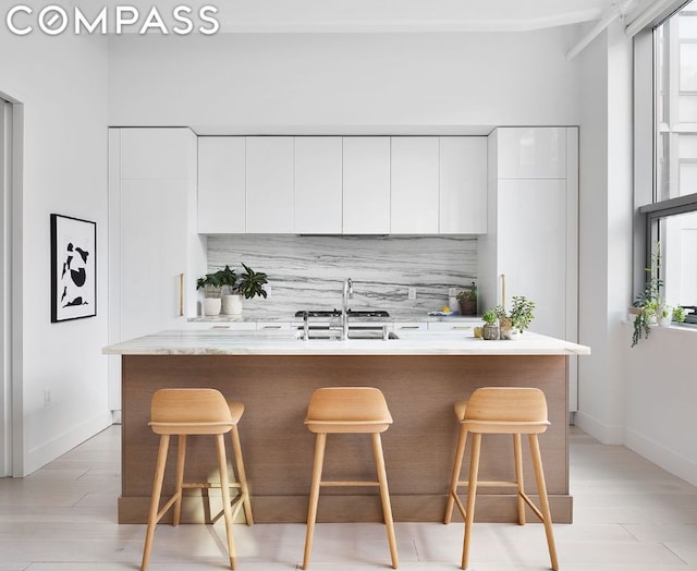 kitchen featuring tasteful backsplash, an island with sink, white cabinets, and a kitchen bar