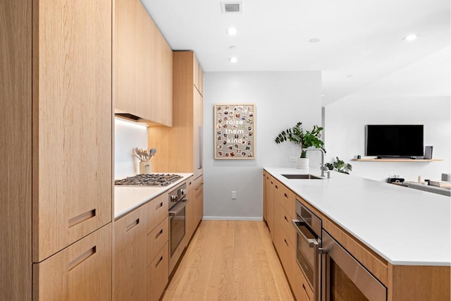 kitchen featuring kitchen peninsula, light hardwood / wood-style floors, sink, appliances with stainless steel finishes, and light brown cabinetry