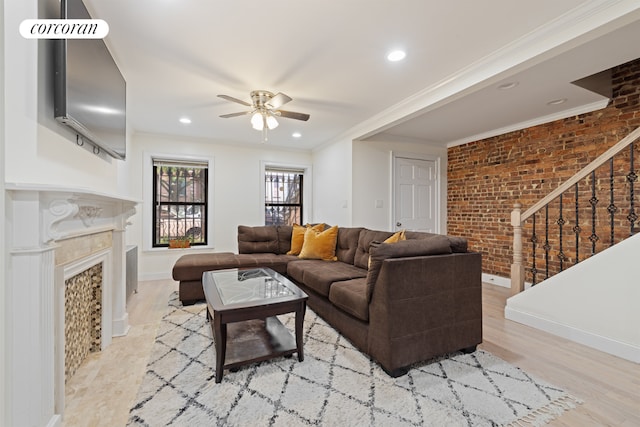 living area with ceiling fan, brick wall, a fireplace, ornamental molding, and stairway