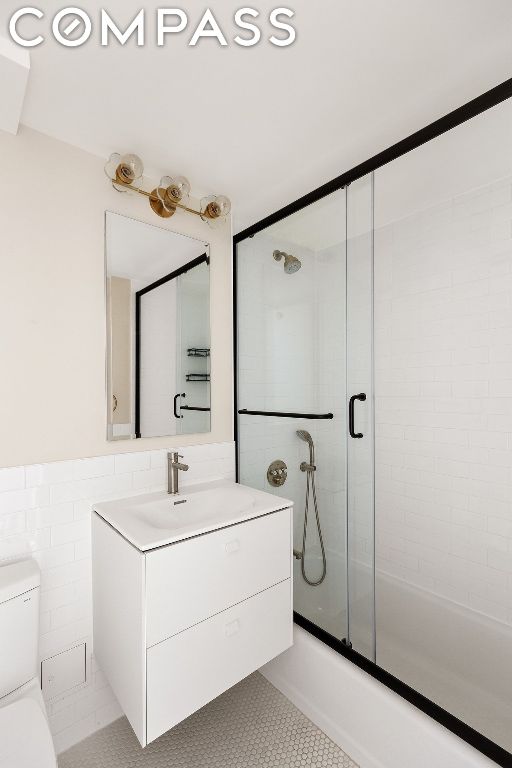 full bathroom featuring shower / bath combination with glass door, tile walls, vanity, tile patterned floors, and toilet