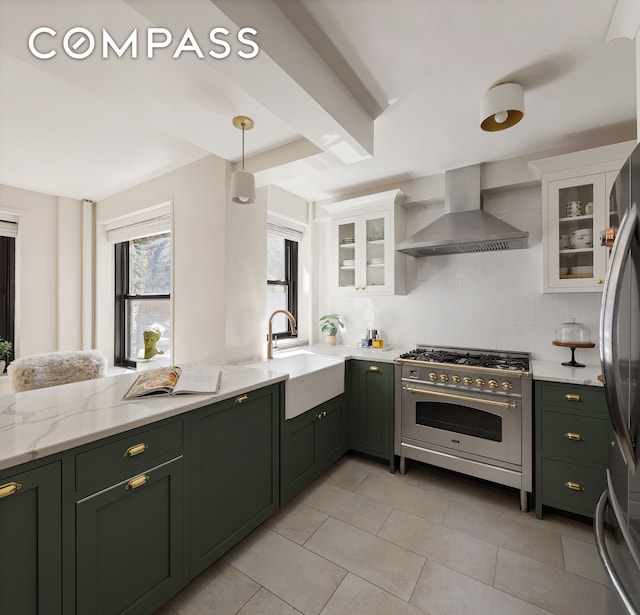 kitchen with wall chimney range hood, white cabinetry, stainless steel appliances, and a sink