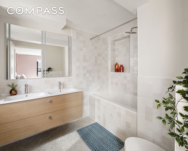 bathroom featuring double vanity, tiled shower / bath combo, a sink, and tile walls