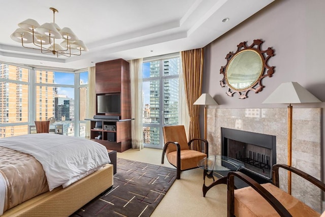 carpeted bedroom with expansive windows, a tiled fireplace, a chandelier, and a raised ceiling