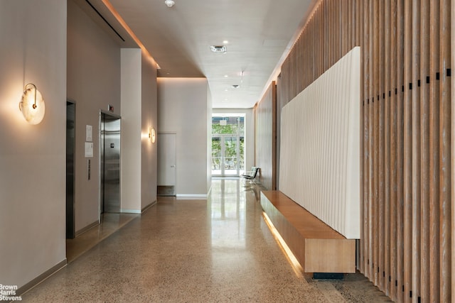 hall featuring visible vents, baseboards, elevator, a towering ceiling, and speckled floor