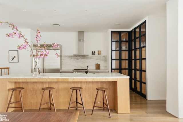 kitchen with stainless steel built in fridge, a kitchen breakfast bar, tasteful backsplash, light wood-style floors, and light countertops