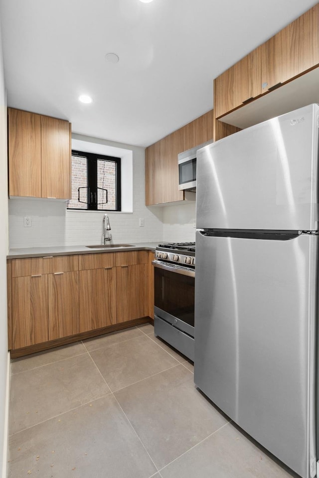 kitchen with appliances with stainless steel finishes, a sink, light tile patterned floors, and light countertops