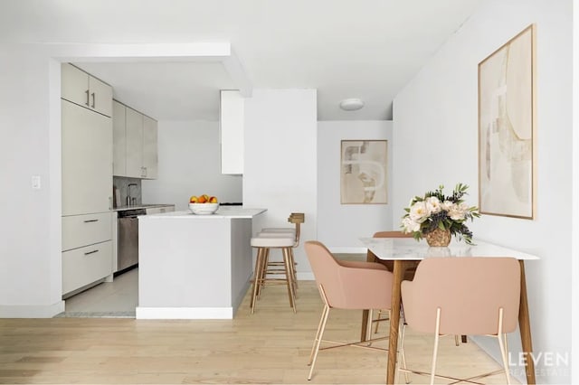 kitchen with light wood-type flooring, white cabinetry, stainless steel dishwasher, kitchen peninsula, and a breakfast bar area