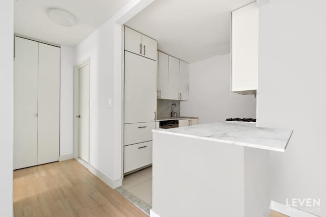 kitchen with a sink, white cabinetry, light countertops, light wood-type flooring, and decorative backsplash