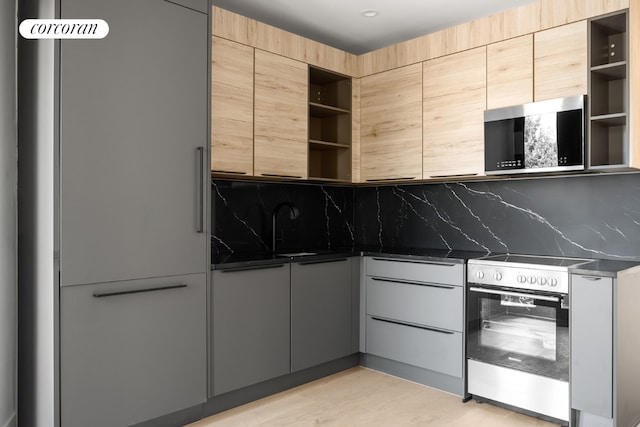 kitchen featuring stainless steel range with electric cooktop, sink, backsplash, dark stone counters, and light brown cabinetry