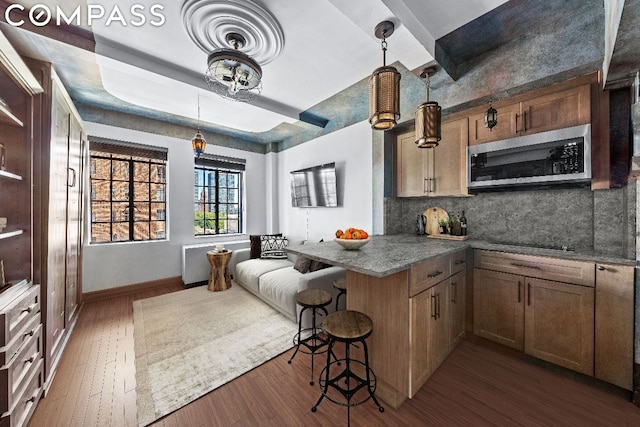 kitchen with black electric cooktop, dark hardwood / wood-style flooring, a kitchen breakfast bar, kitchen peninsula, and backsplash