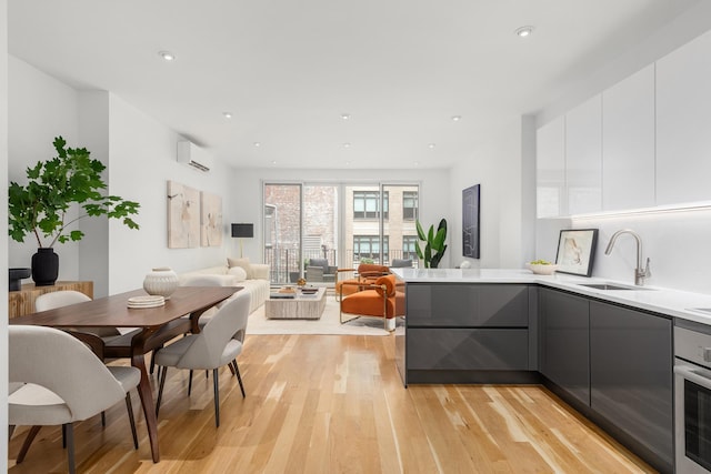 kitchen with an AC wall unit, light wood finished floors, modern cabinets, and a sink