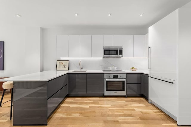 kitchen with white cabinetry, stainless steel appliances, a kitchen breakfast bar, kitchen peninsula, and gray cabinetry