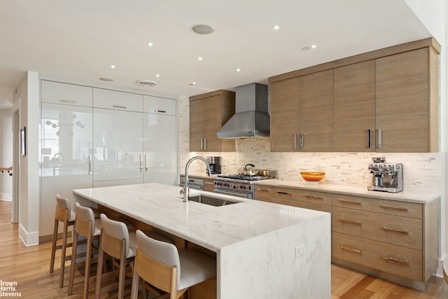 kitchen featuring a sink, backsplash, light wood-style floors, wall chimney exhaust hood, and high end range